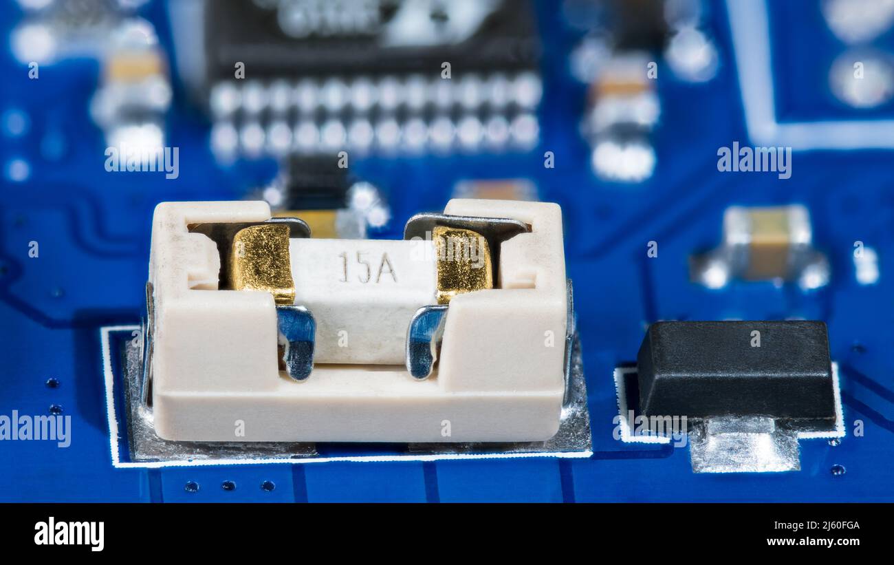 Small electrical fuse in white holder and black linear fixed voltage regulator on blue PCB. Printed circuit board detail with surface mount technology. Stock Photo
