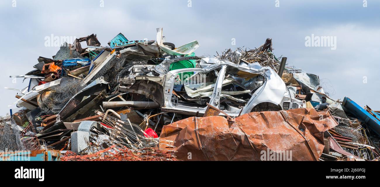 Closeup of mixed scrap metal pile in junkyard on panoramic blue sky background. Colored jumble of iron waste as old car body, wire mesh or rusty sheet. Stock Photo