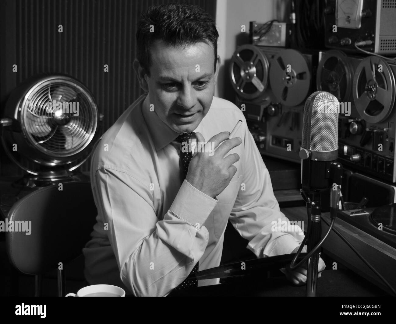 A Cool 1950's 60's Retro Radio DJ host plays music while holding record and cigarette. A classic black and white image from a bygone era. Nostalgia. Stock Photo