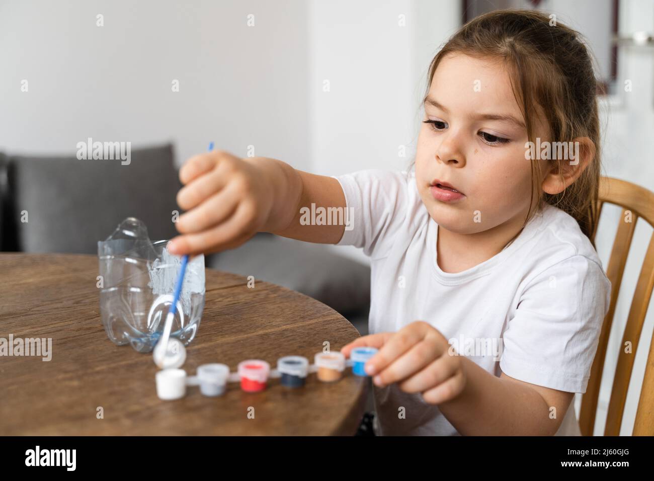 Caucasian preschool girl doing crafts with plastic bottle and paints ...