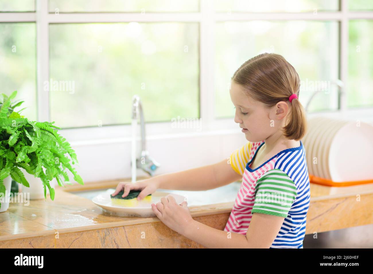 https://c8.alamy.com/comp/2J60HEF/child-washing-dishes-home-chores-kid-in-white-kitchen-cleaning-plates-after-lunch-at-window-2J60HEF.jpg