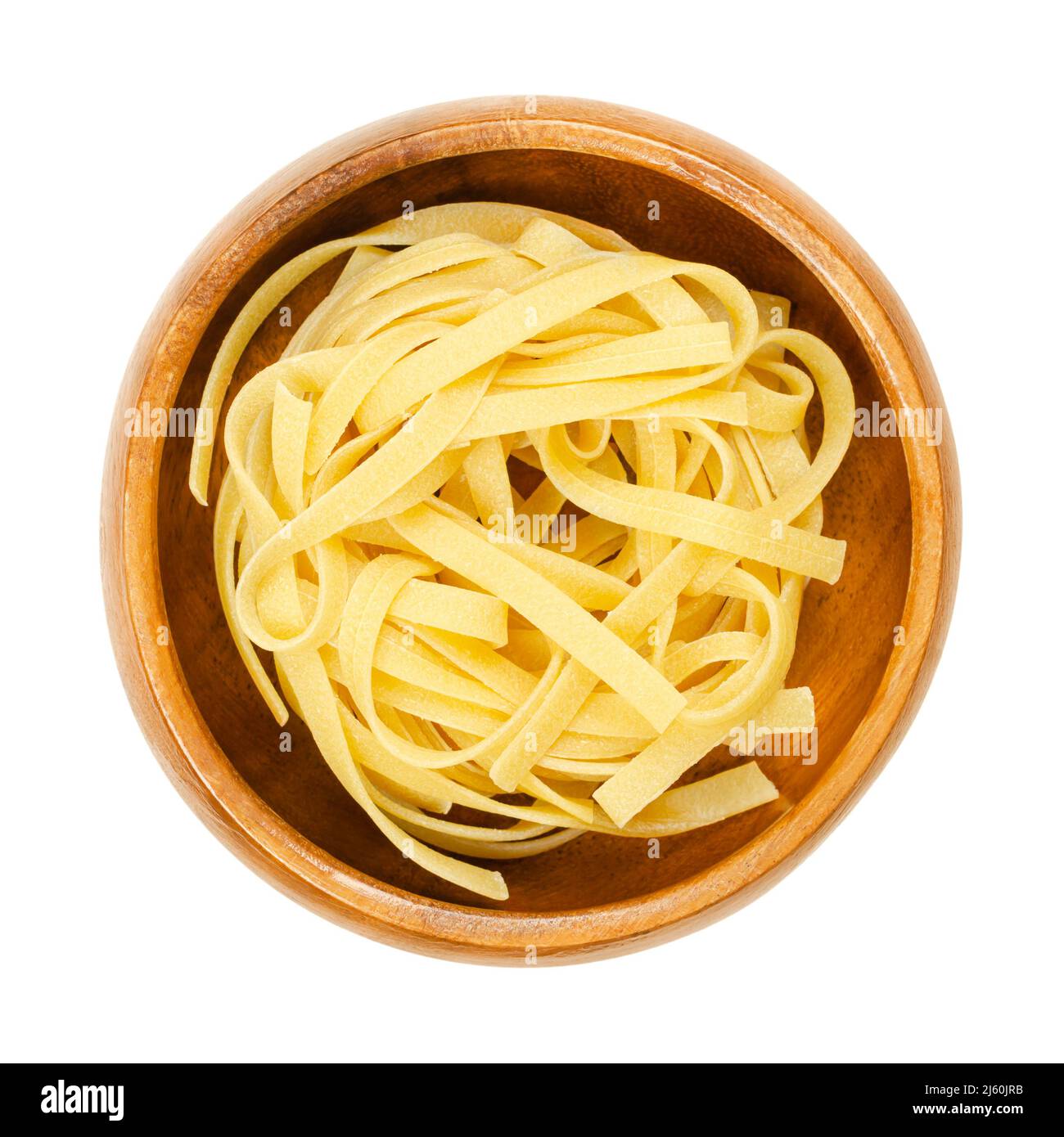 Uncooked, dried tagliatelle pasta, in a wooden bowl. Traditional type of egg pasta, from the Emilia-Romagna and Marche regions in Italy. Stock Photo