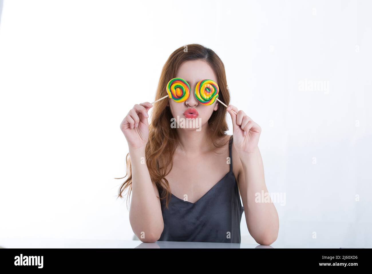 Pretty young lady playfully shielded her eyes with two colorful lollipops, on white background - stock photo Stock Photo