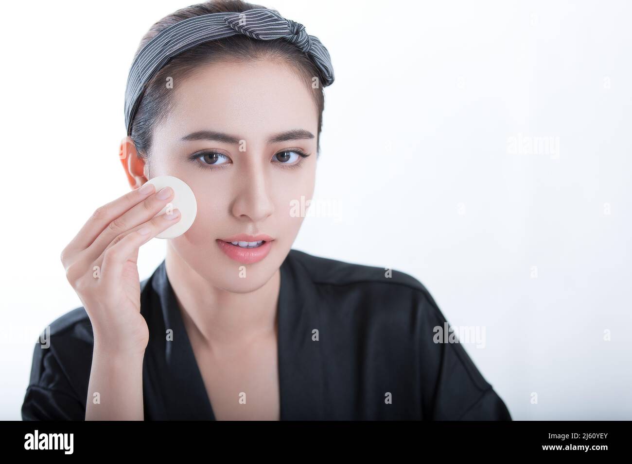 Beautiful young Chinese woman is using powder to make up, on white background - stock photo Stock Photo