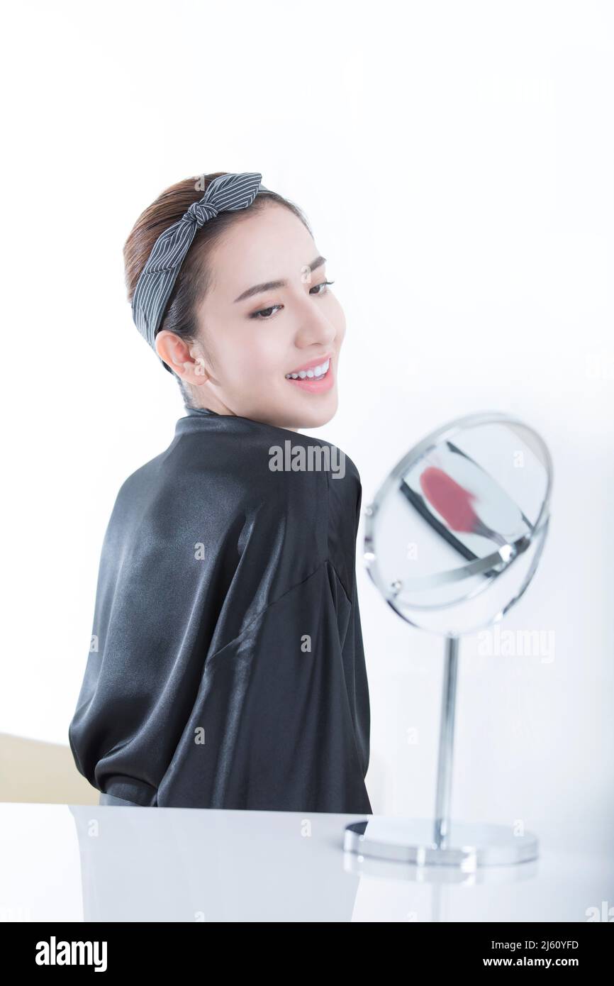 An elegant young Chinese woman looking at her shoulders in a makeup mirror, on white background - stock photo Stock Photo