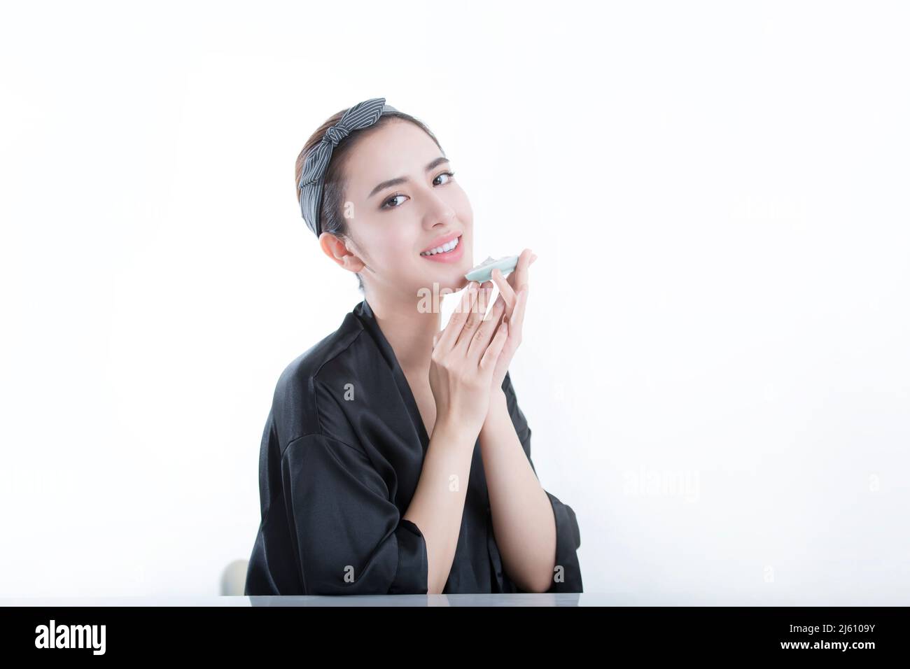 Beautiful young Chinese skin nurse testing rich aroma of beauty treatment product, on white background - stock photo Stock Photo