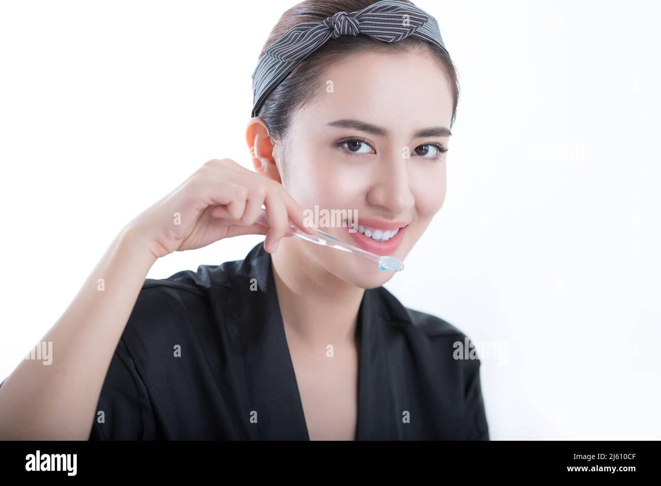 Beautiful young Chinese woman using a toothbrush to clean and whitening her teeth, on white background - stock photo Stock Photo