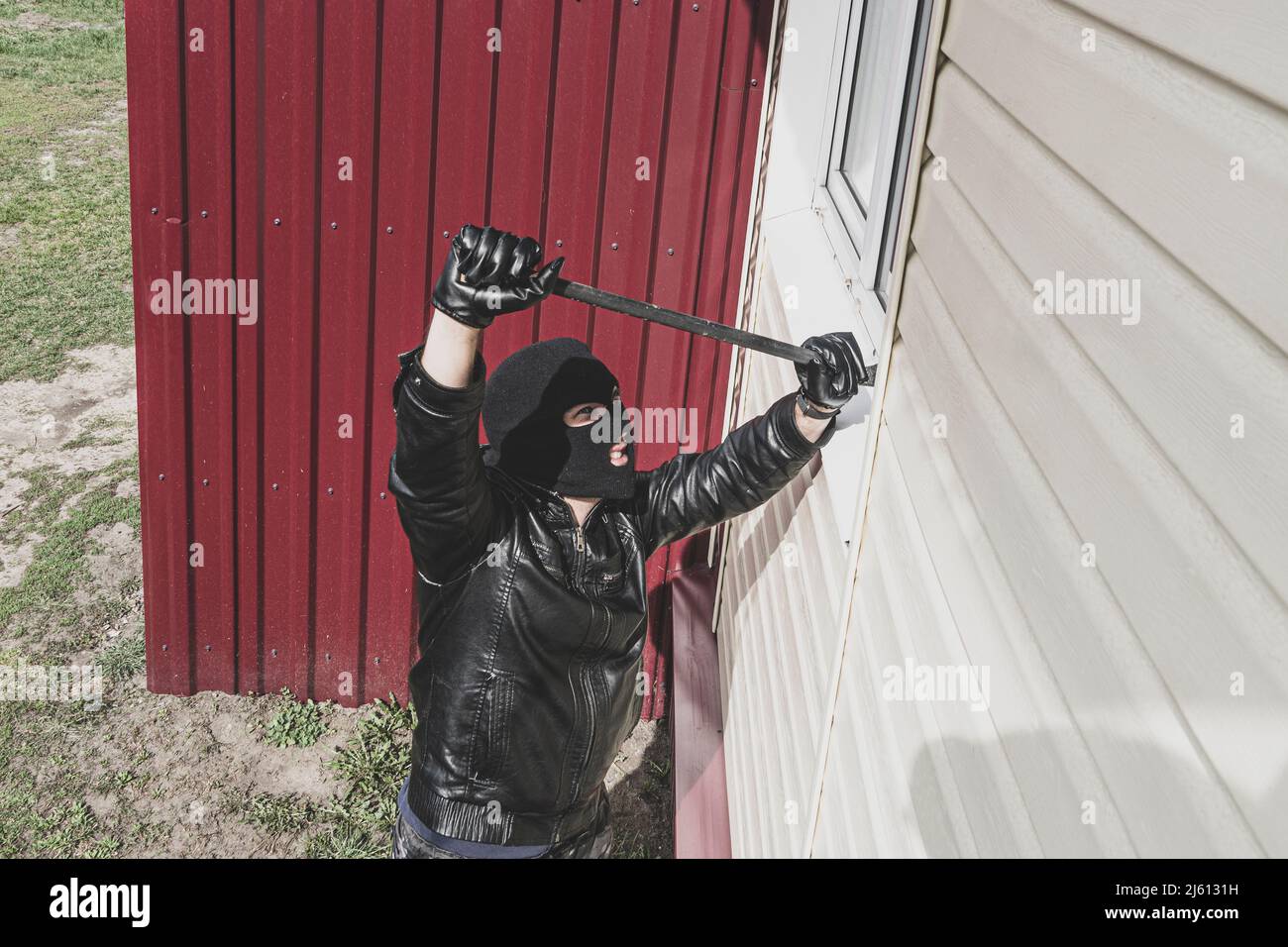 Thief in balaclava breaking glass of window to enter the house. A ...