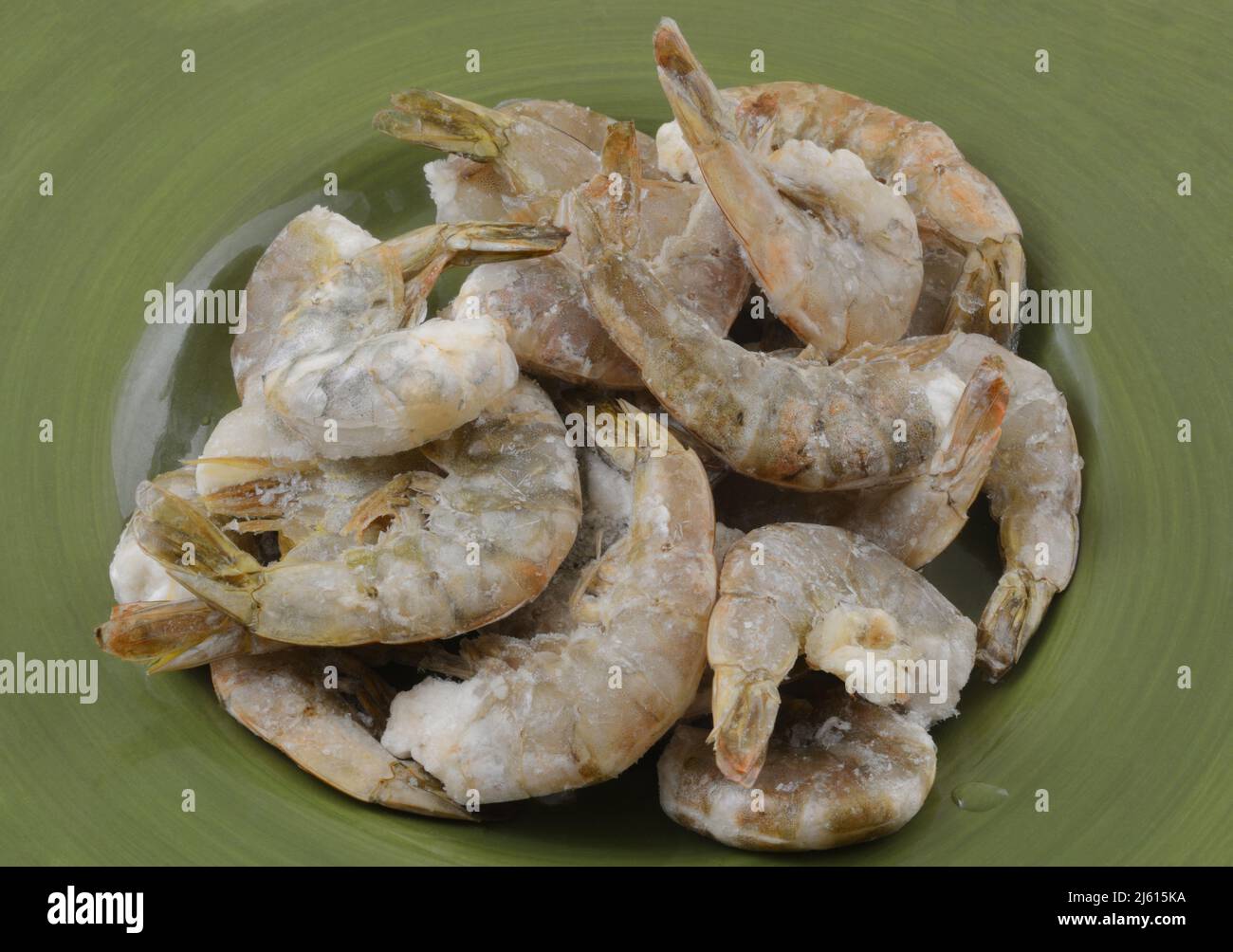 Freezer burned shrimp in the shell coated with ice crystals from improper packaging or refrigeration thawing on green plate Stock Photo