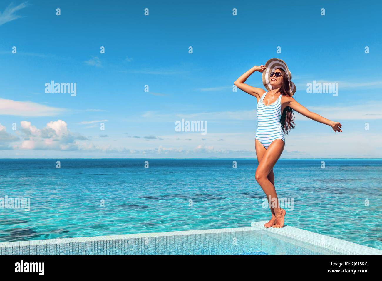 Travel vacation tourist woman relaxing at infinity pool in French Polynesia. Happy woman in swimsuit and sun hat over blue ocean at luxury resort Stock Photo