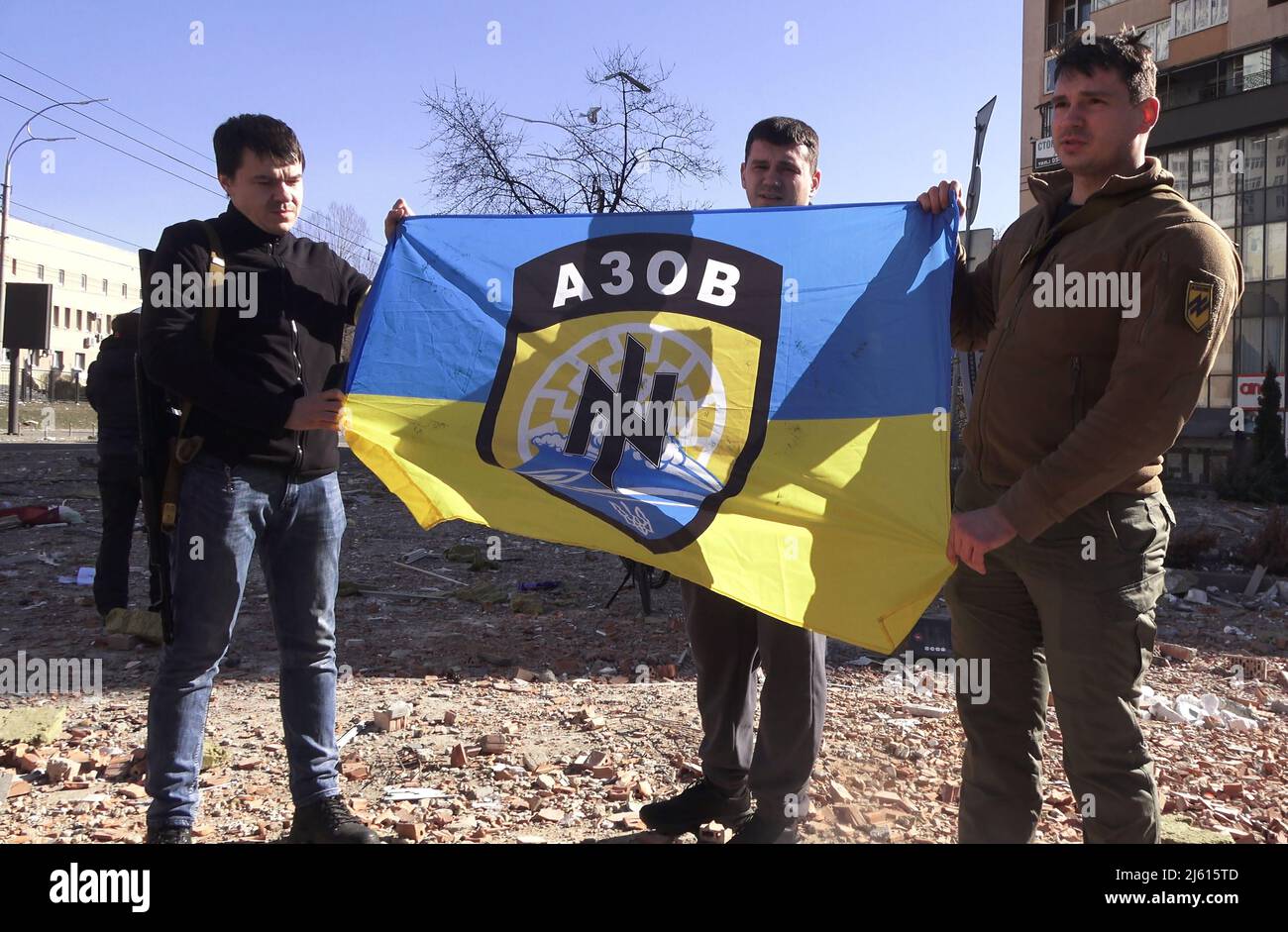 KYIV, UKRAINE 28 FEBRUARY. Azov affiliated volunteers hold their far right battalion flag at the site of a damaged residential building following a rocket attack on 28 February 2022 in Kiev, Ukraine. Azov is a far-right all-volunteer infantry military unit whose members, estimated at 900, are ultra-nationalists and accused of harbouring neo-Nazi and white supremacist ideology. Russia began a military invasion of Ukraine after Russia's parliament approved treaties with two breakaway regions in eastern Ukraine. It is the largest military conflict in Europe since World War II. Stock Photo