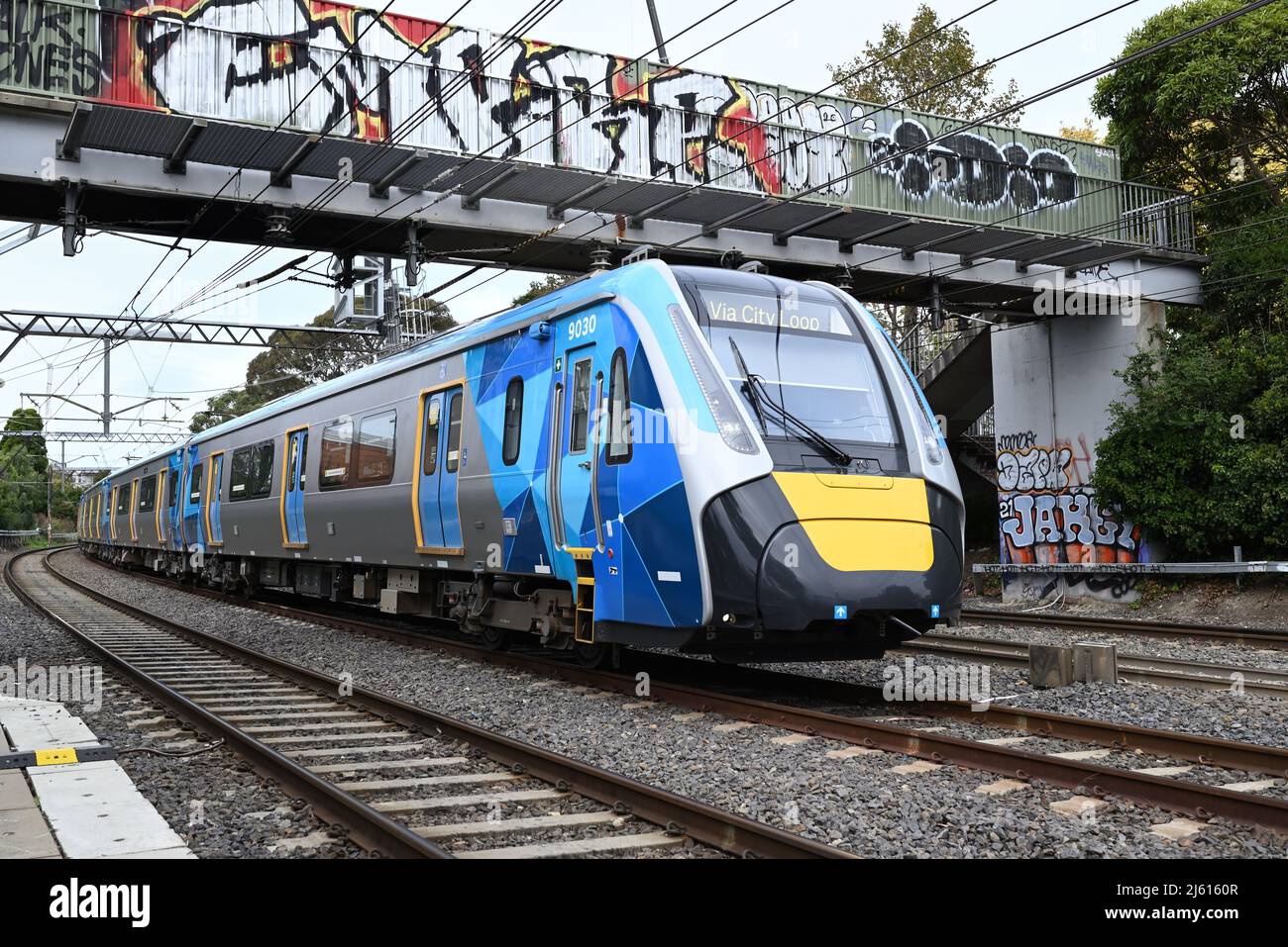 City bound High Capacity Metro Train passing under a footbridge in the inner suburbs of Melbourne on an overcast day Stock Photo