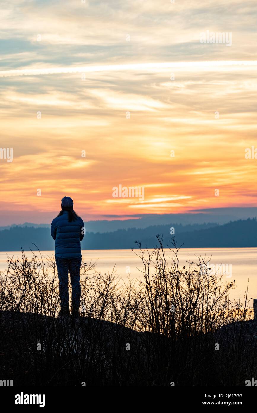Woman watching the sunset over the Salish Sea from Saxe Point Park in Esquimalt - Victoria, Vancouver Island, British Columbia, Canada Stock Photo