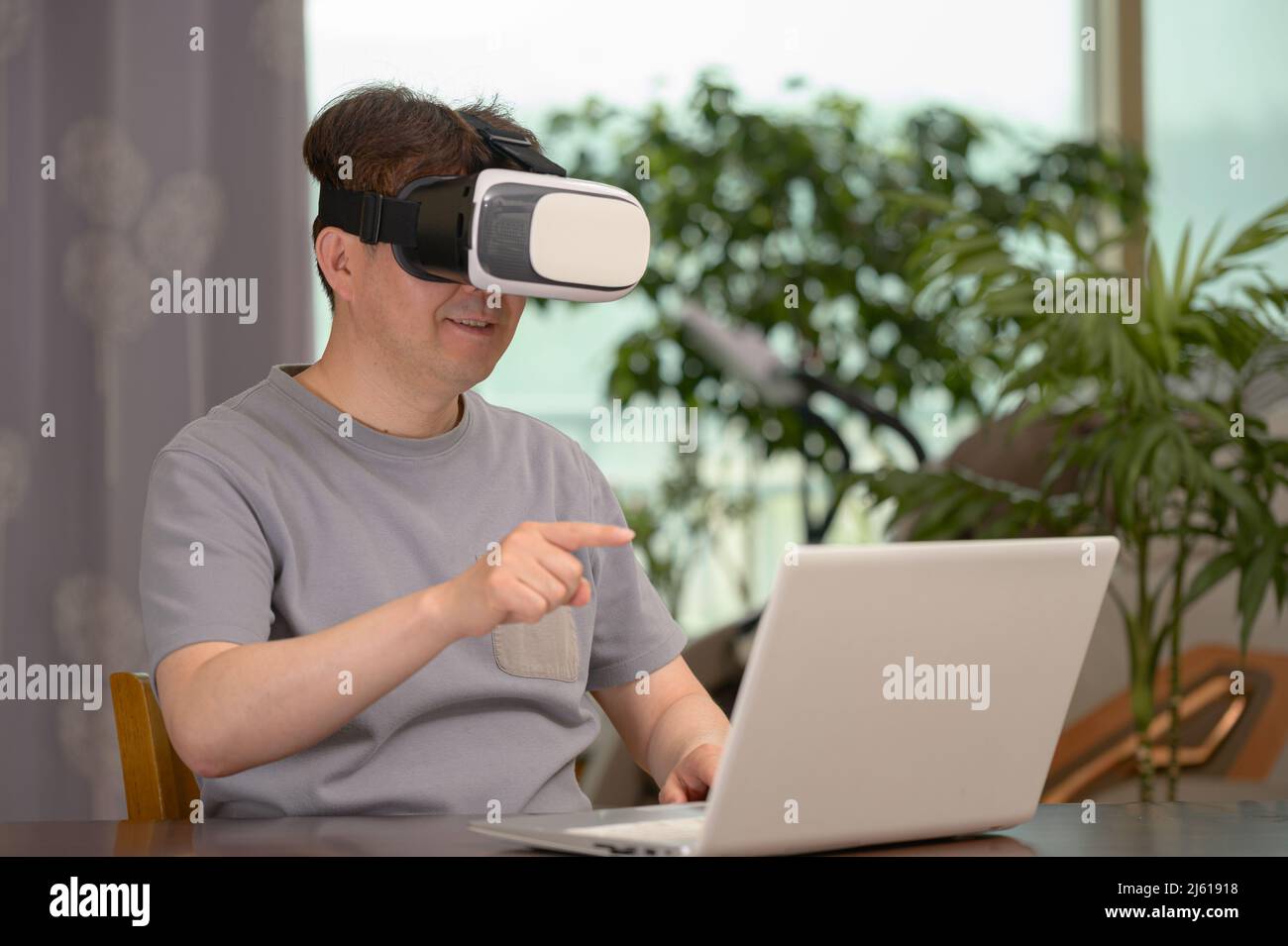Asian man wearing VR headset and using laptop while sitting at his desk Stock Photo
