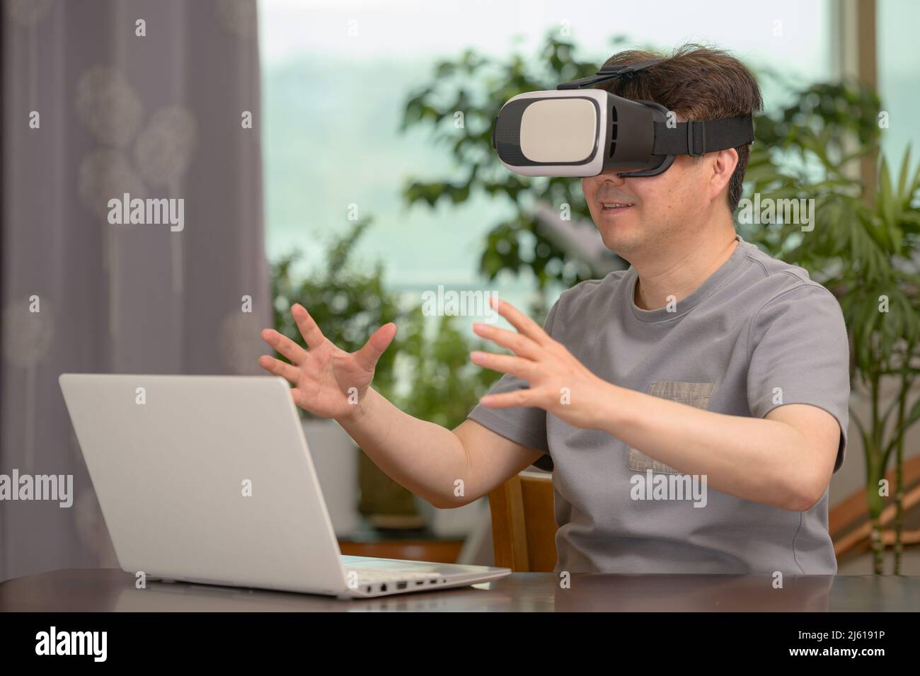 Asian man wearing VR headset and using laptop while sitting at his desk Stock Photo