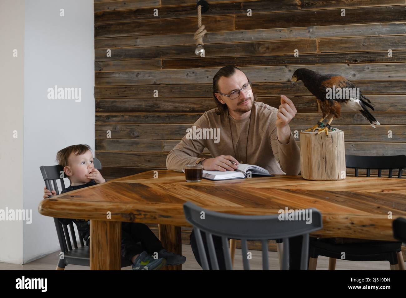 Man is working, writing with wild bird at home by the table, child sitting.  Making noted, memories, diary with eagle as pet. Unusual animals. Human  Stock Photo - Alamy
