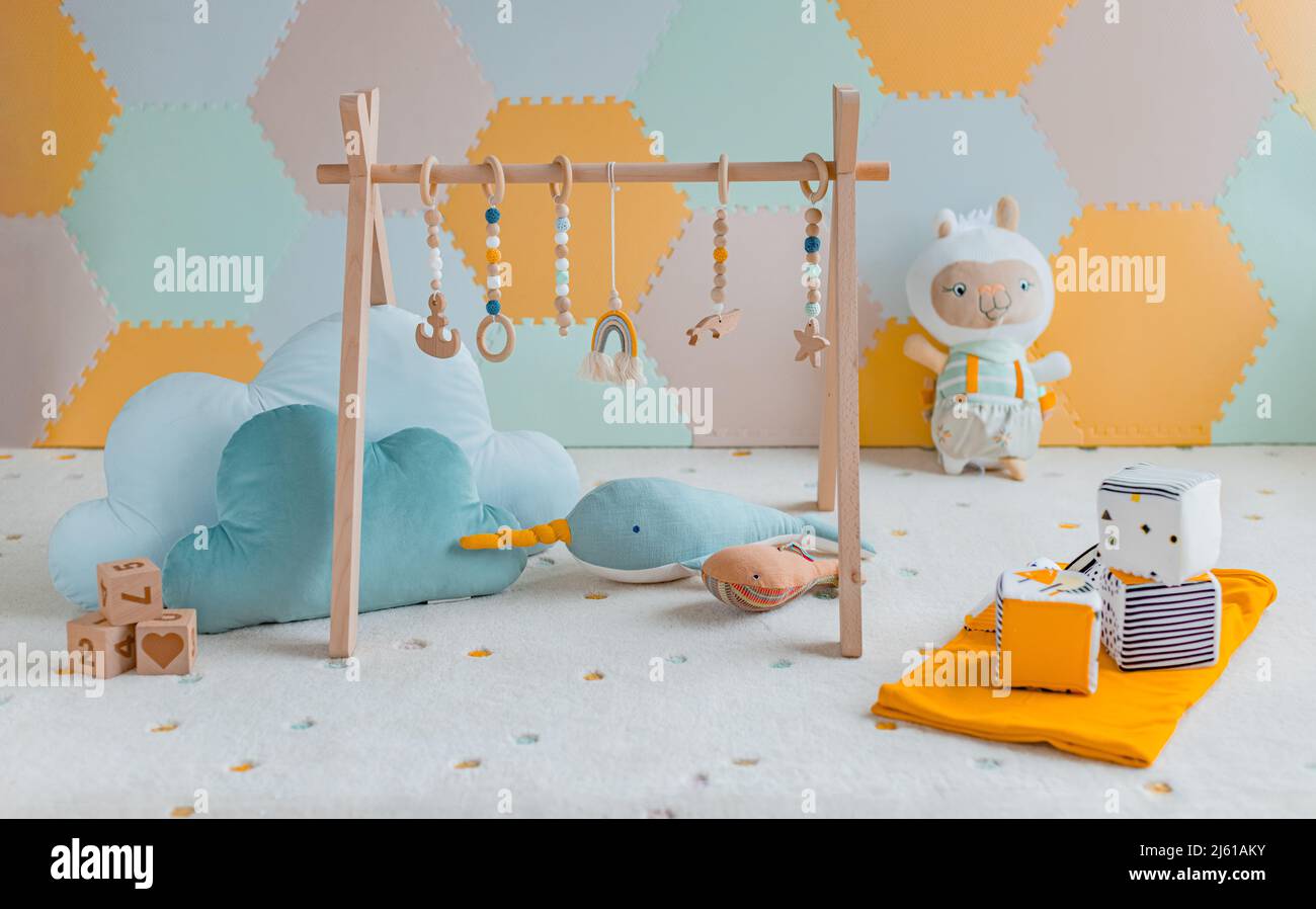 Baby activity gym play toys hanging from wooden arch on playmat in nursery or playroom. Home decoration children objects with learning cubes, plush Stock Photo