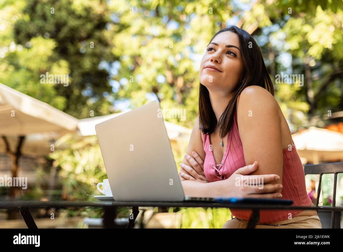 Thoughtful caucasian woman with laptop looking away sitting in outdoors terrace Stock Photo