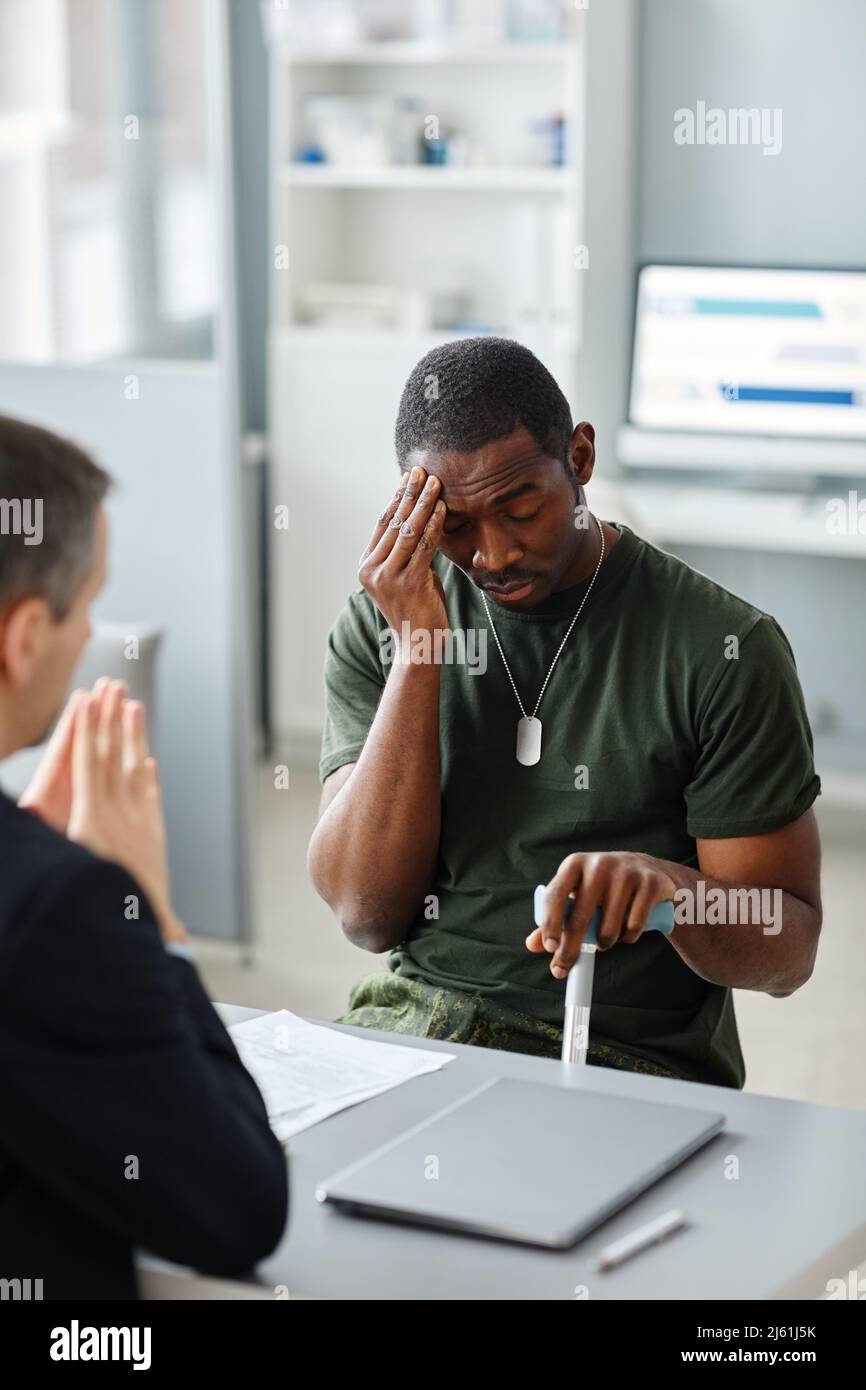 Young African American soldier with walking stick sitting in front of psychotherapist complaining about chronic stress headaches Stock Photo