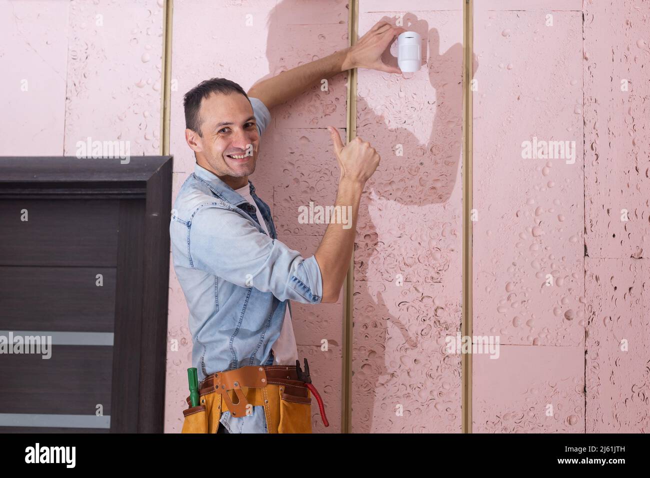Young electrician installing security alarm on wall. Stock Photo
