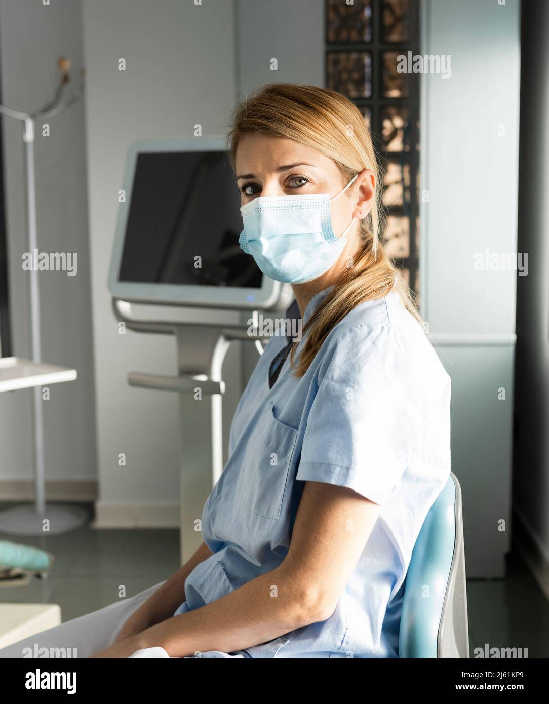 Dentist with protective face mask sitting on chair at dental clinic Stock Photo
