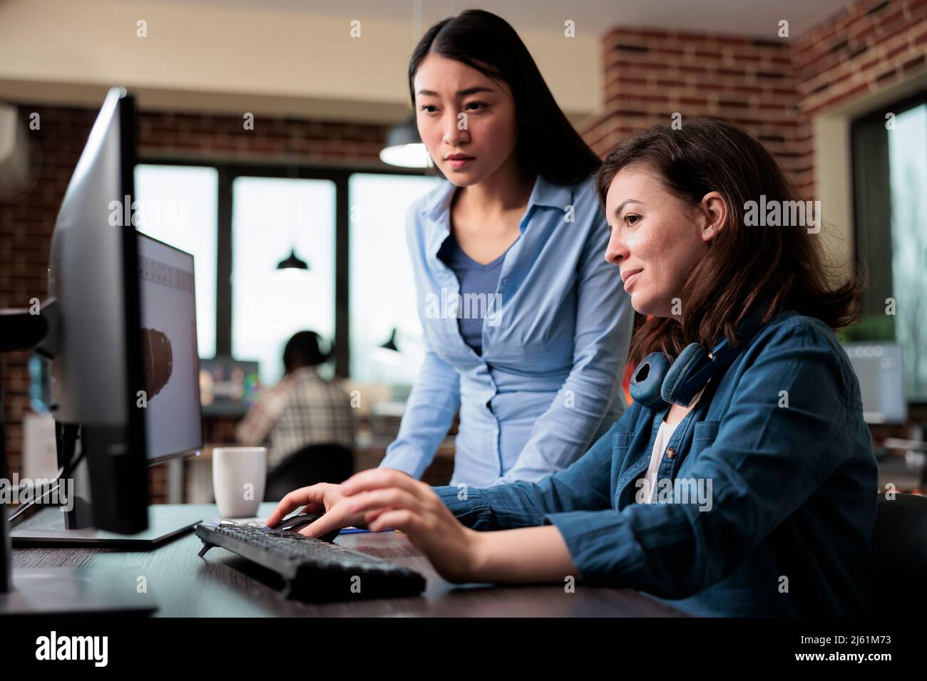 Creative designers developing digital arts on PC while discussing about 3D technology. Professional office workers pointing out wrong blueprint of project while using work computer. Stock Photo