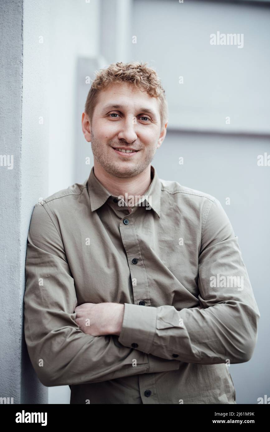 Happy businessman with arms crossed leaning on wall Stock Photo - Alamy