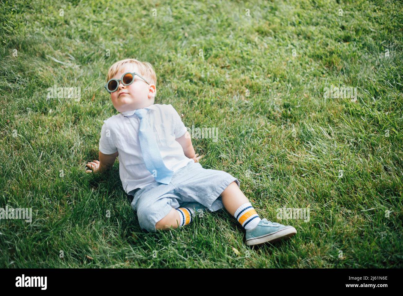 Boy wearing sunglasses and necktie sitting on grass Stock Photo Alamy
