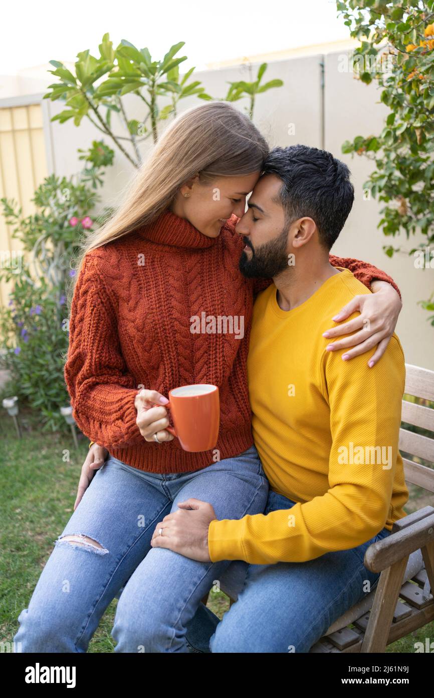 Woman with coffee cup sitting on man's lap in garden Stock Photo