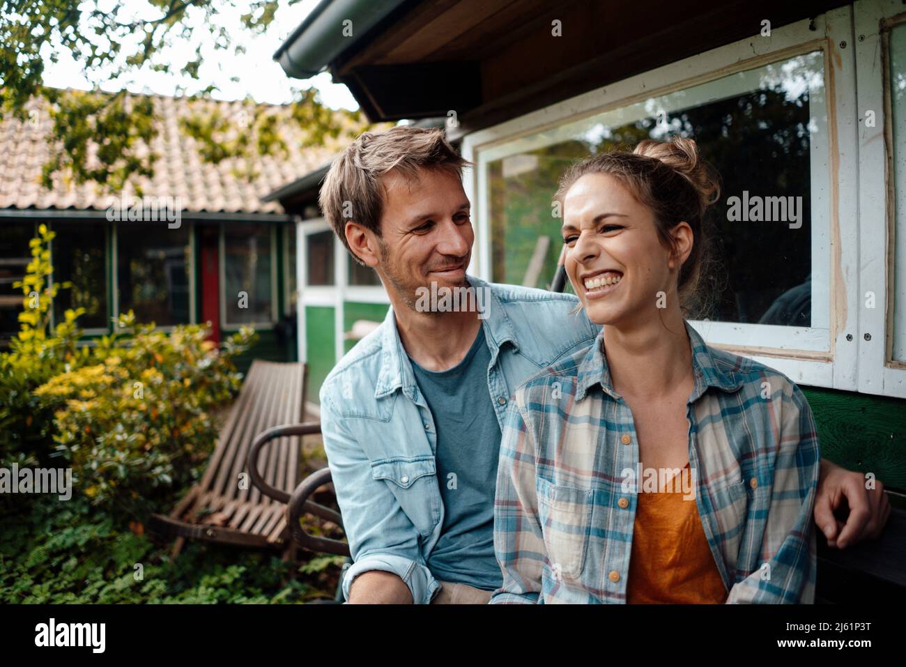 Smiling man looking at happy girlfriend sitting at backyard Stock Photo