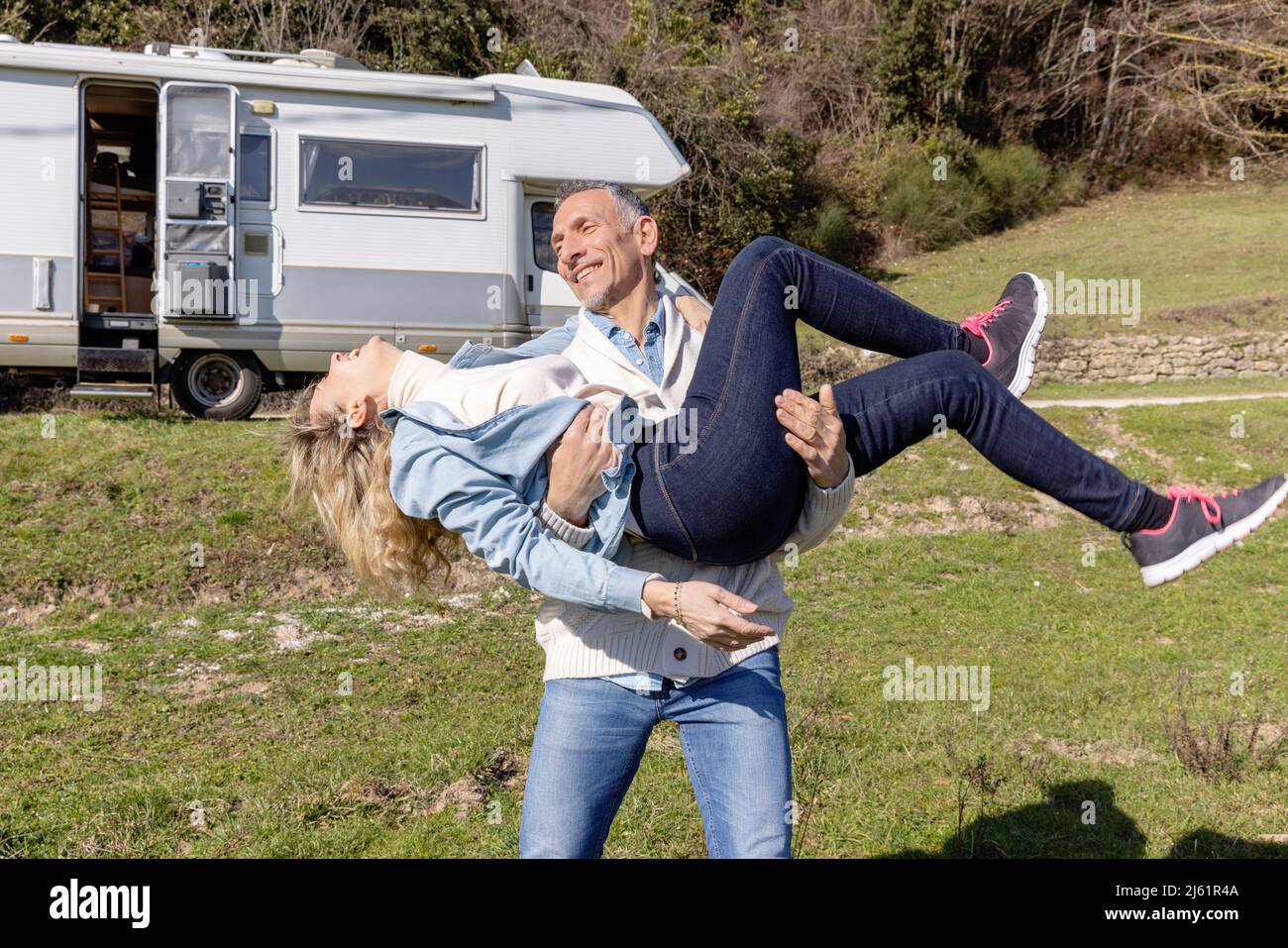 Man carrying woman standing in front of camper van Stock Photo