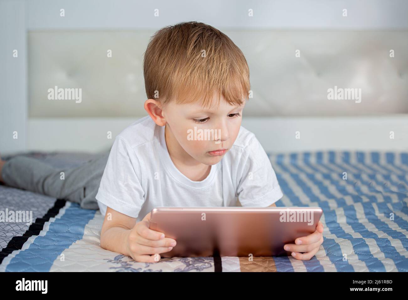 Kids and gadgets. The boy is lying on the bed and looking at the tablet ...
