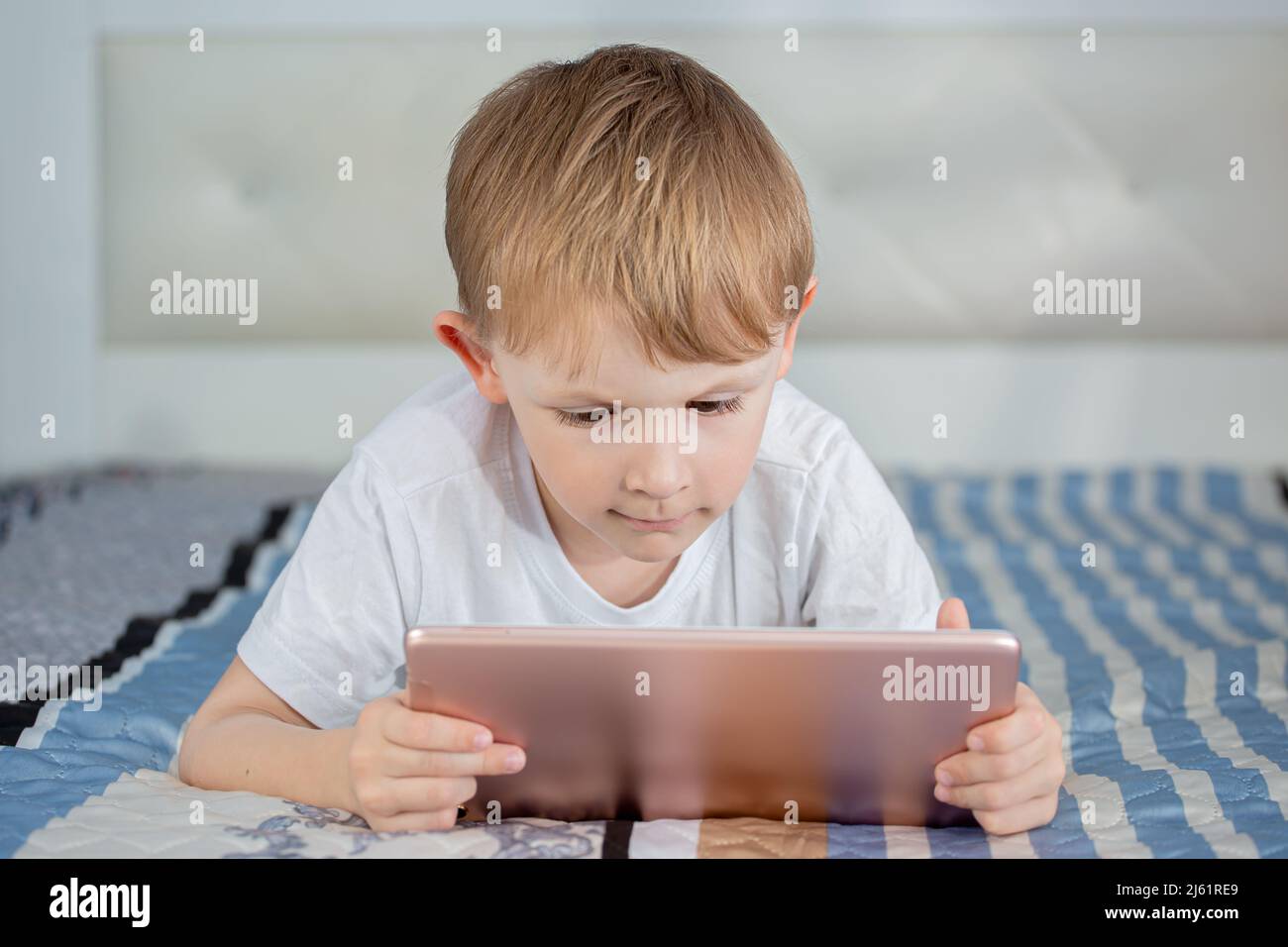 Kids and gadgets. The boy is lying on the bed and looking at the tablet ...