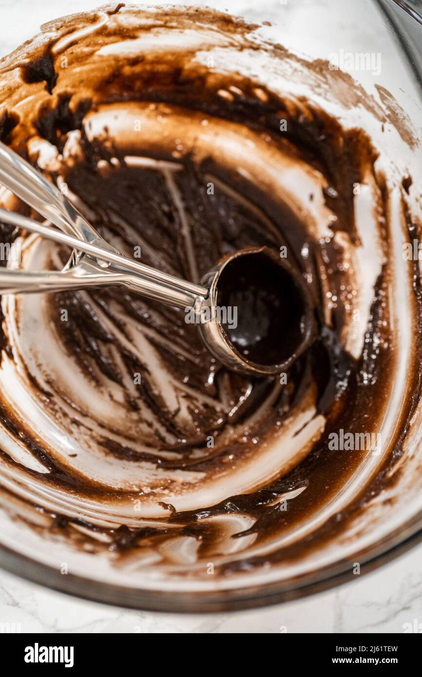 Scooping cake batter with dough scoop into cupcake foil liners to bake