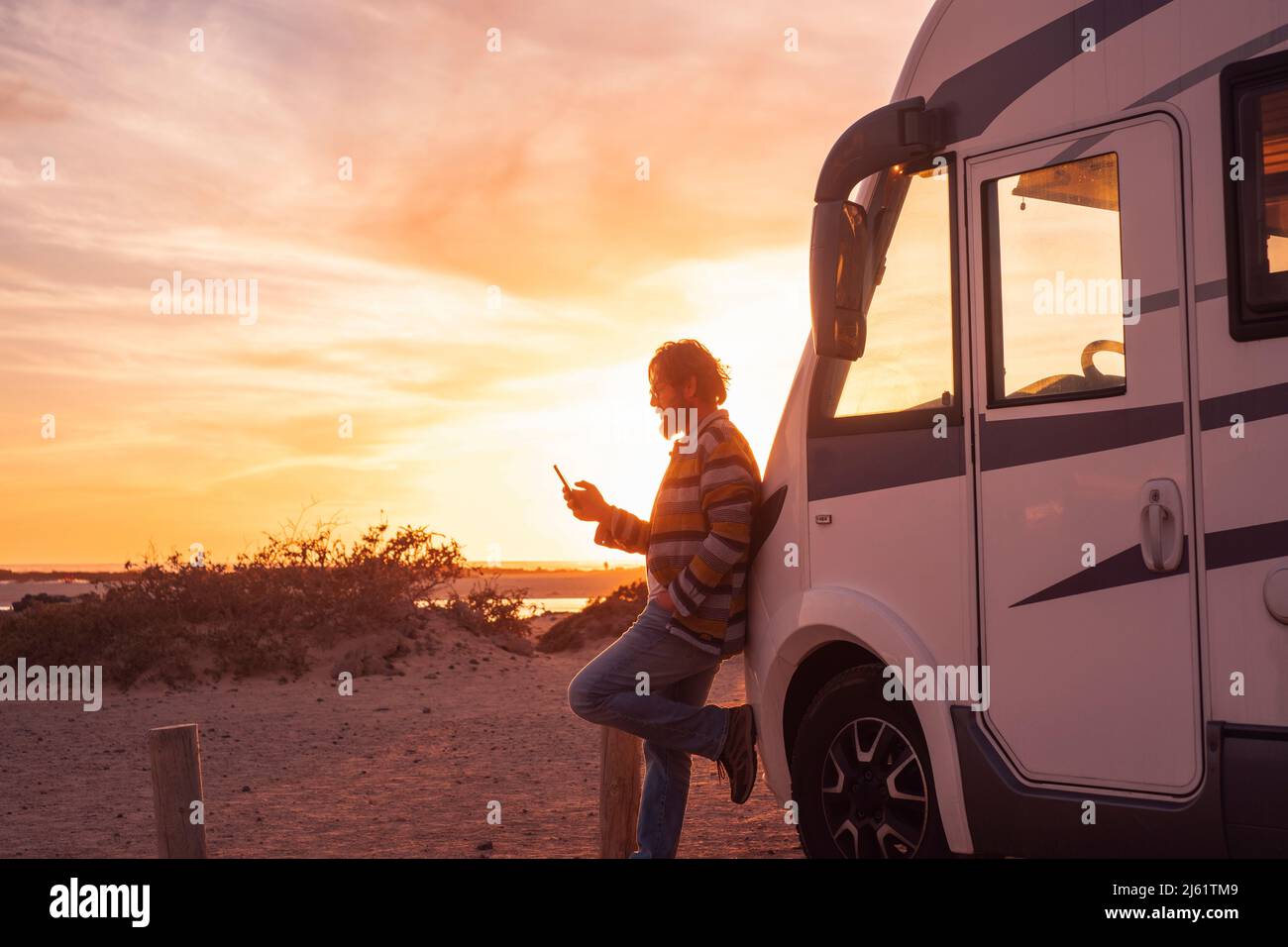 Man leaning on camper van and using smart phone Stock Photo