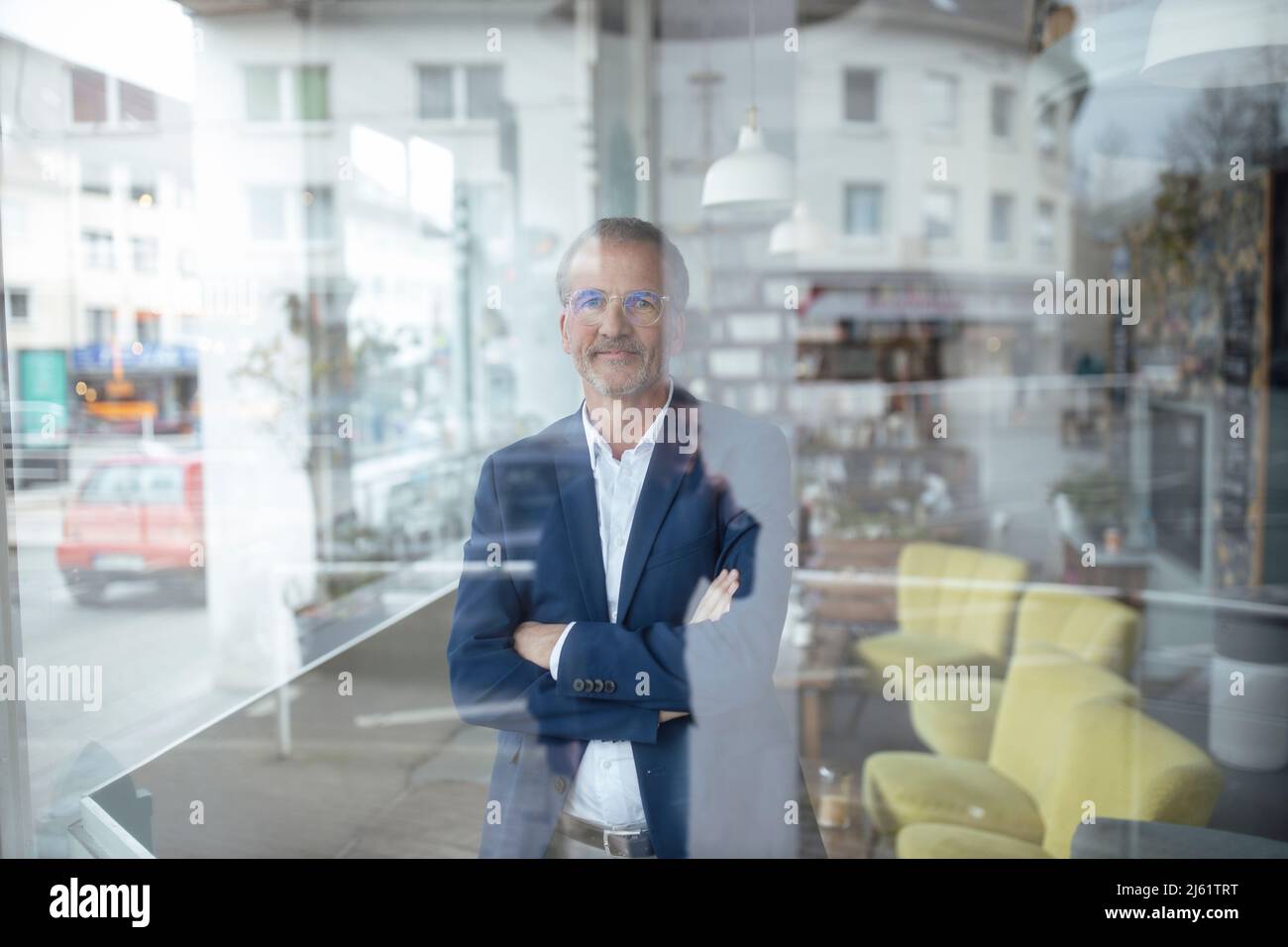 Smiling businessman with arms crossed seen through glass window at cafe ...