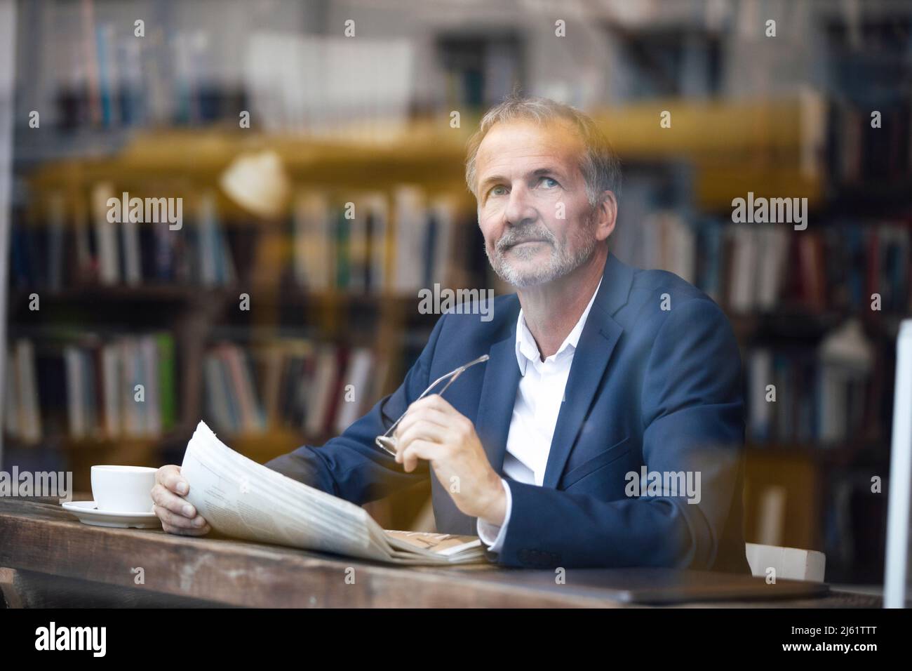 Thoughtful businessman with eyeglasses and newspaper sitting at table in cafe Stock Photo