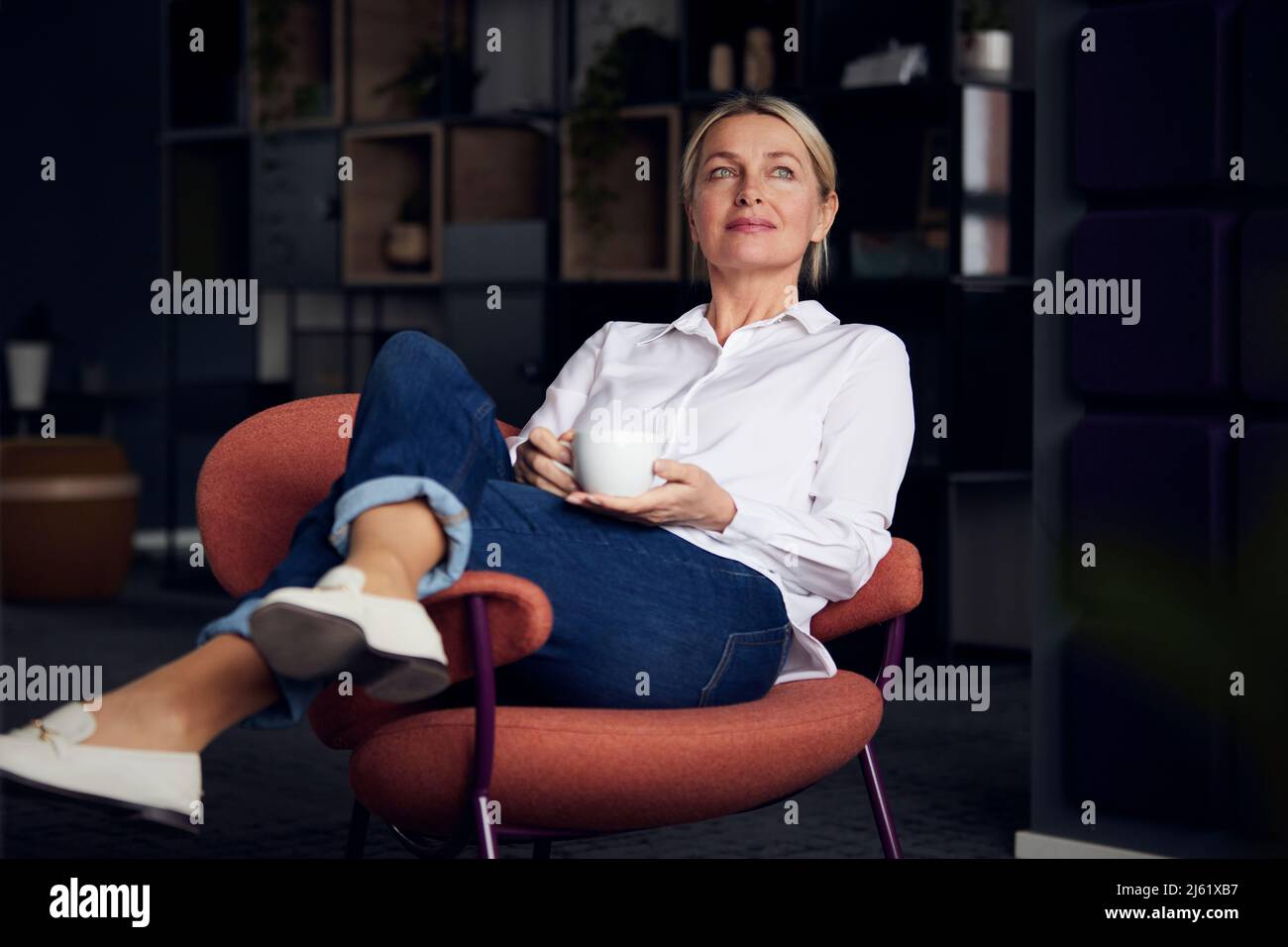 Businesswoman holding coffee cup sitting with legs crossed at knee on chair Stock Photo