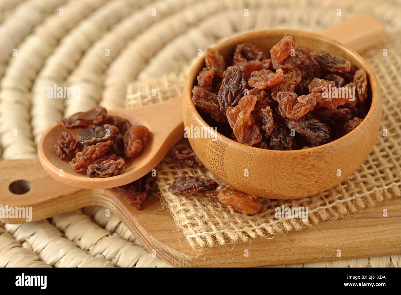 Close-up of raisins in wooden bowl and spoon on wooden chopping board Stock Photo