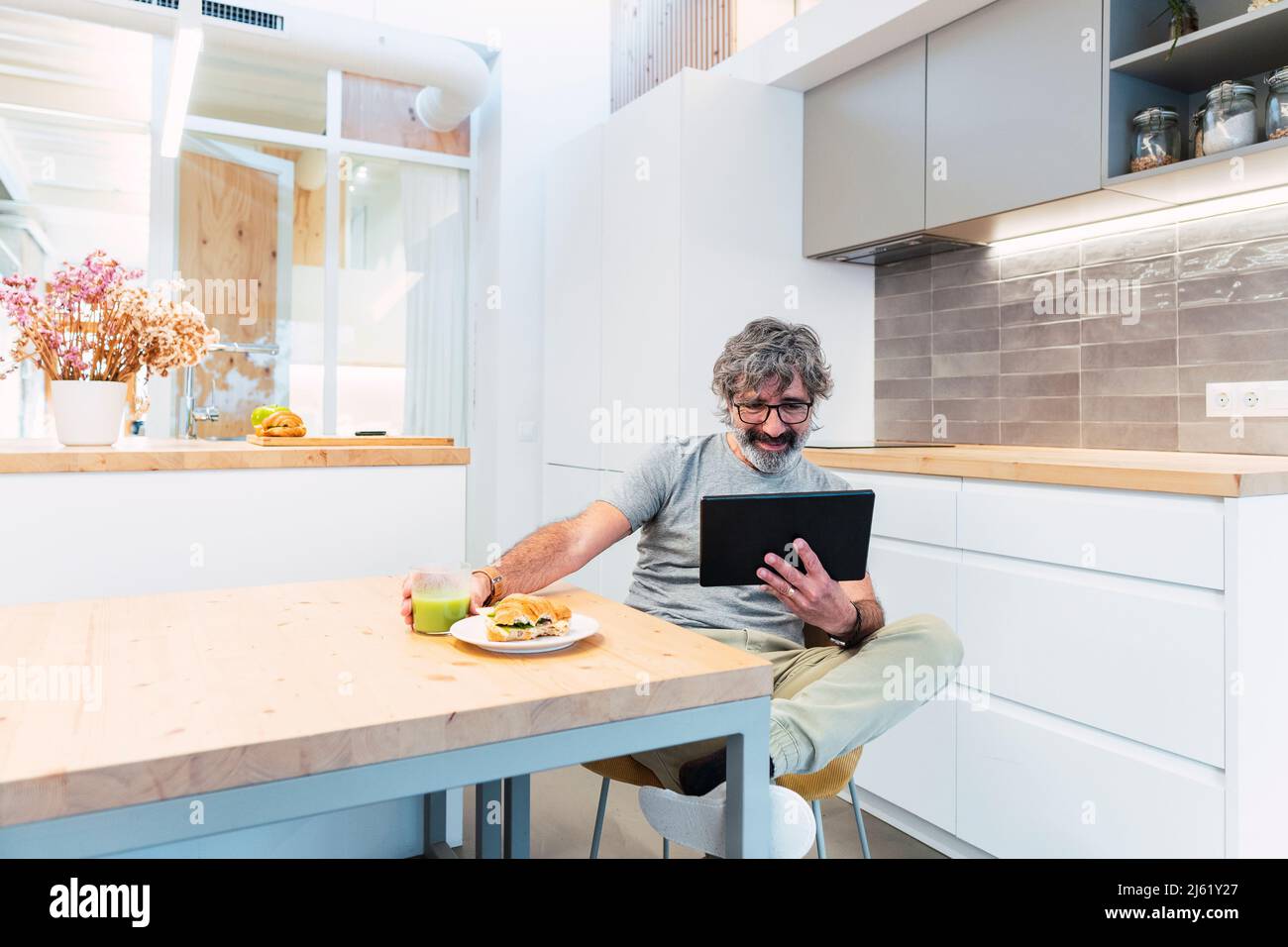 Man sitting at table using tablet PC and having breakfast at home Stock Photo