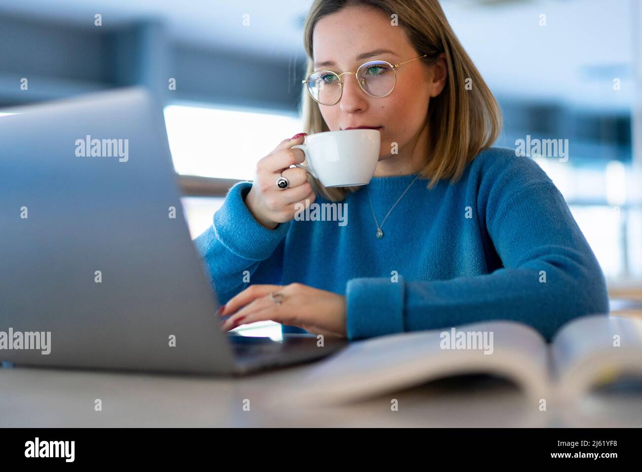 Young woman drinking coffee and using laptop at table Stock Photo