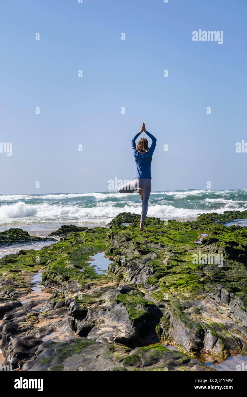 Woman standing on rock practicing tree pose doing yoga at beach Stock ...