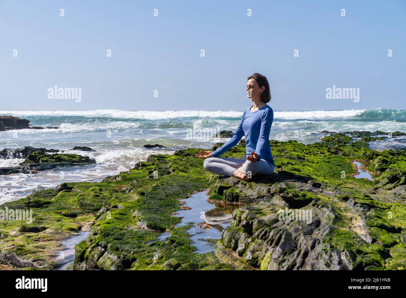 Woman sitting in lotus position and meditating on rock at beach Stock ...