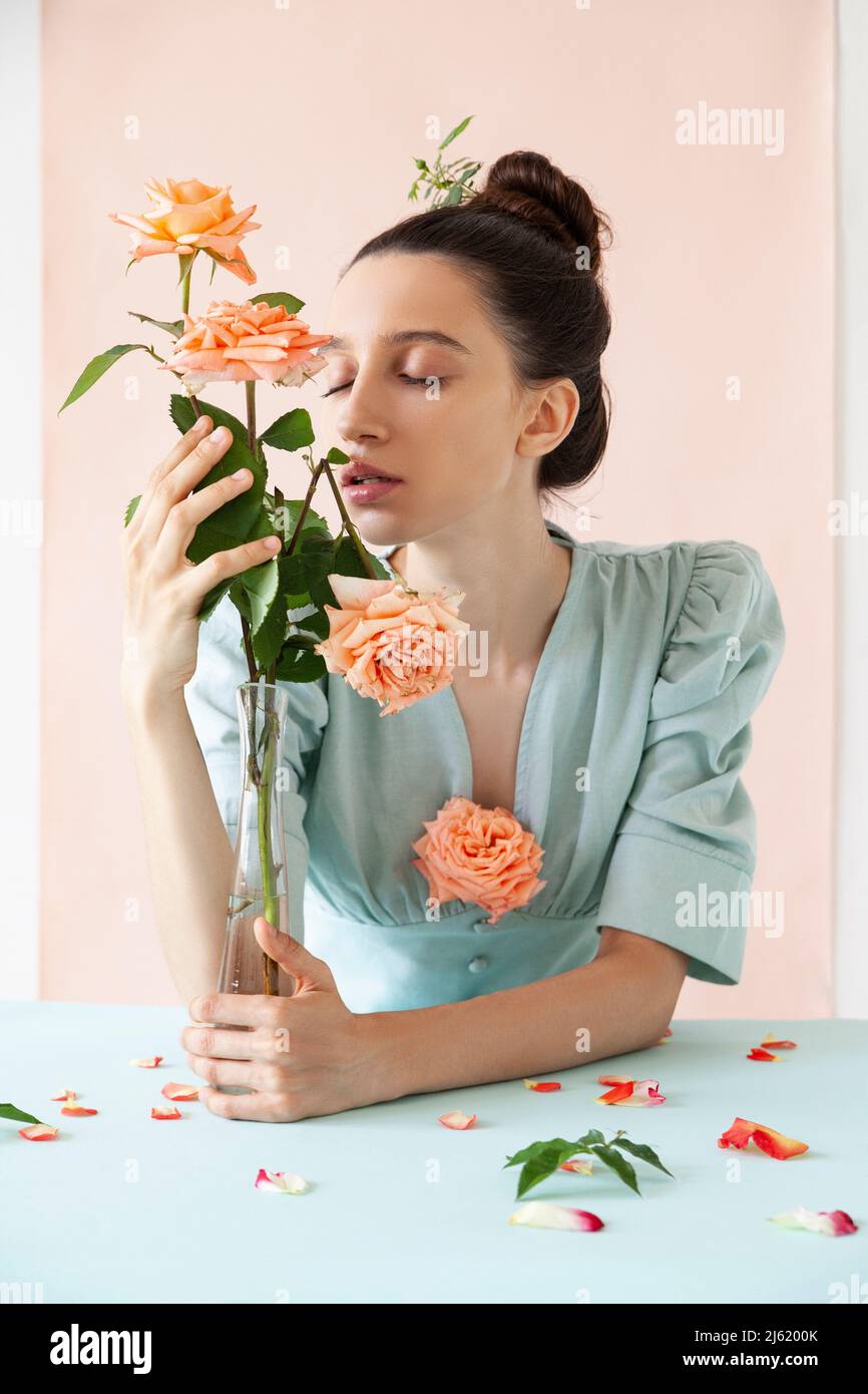 Young woman with eyes closed smelling rose against pink backdrop Stock Photo