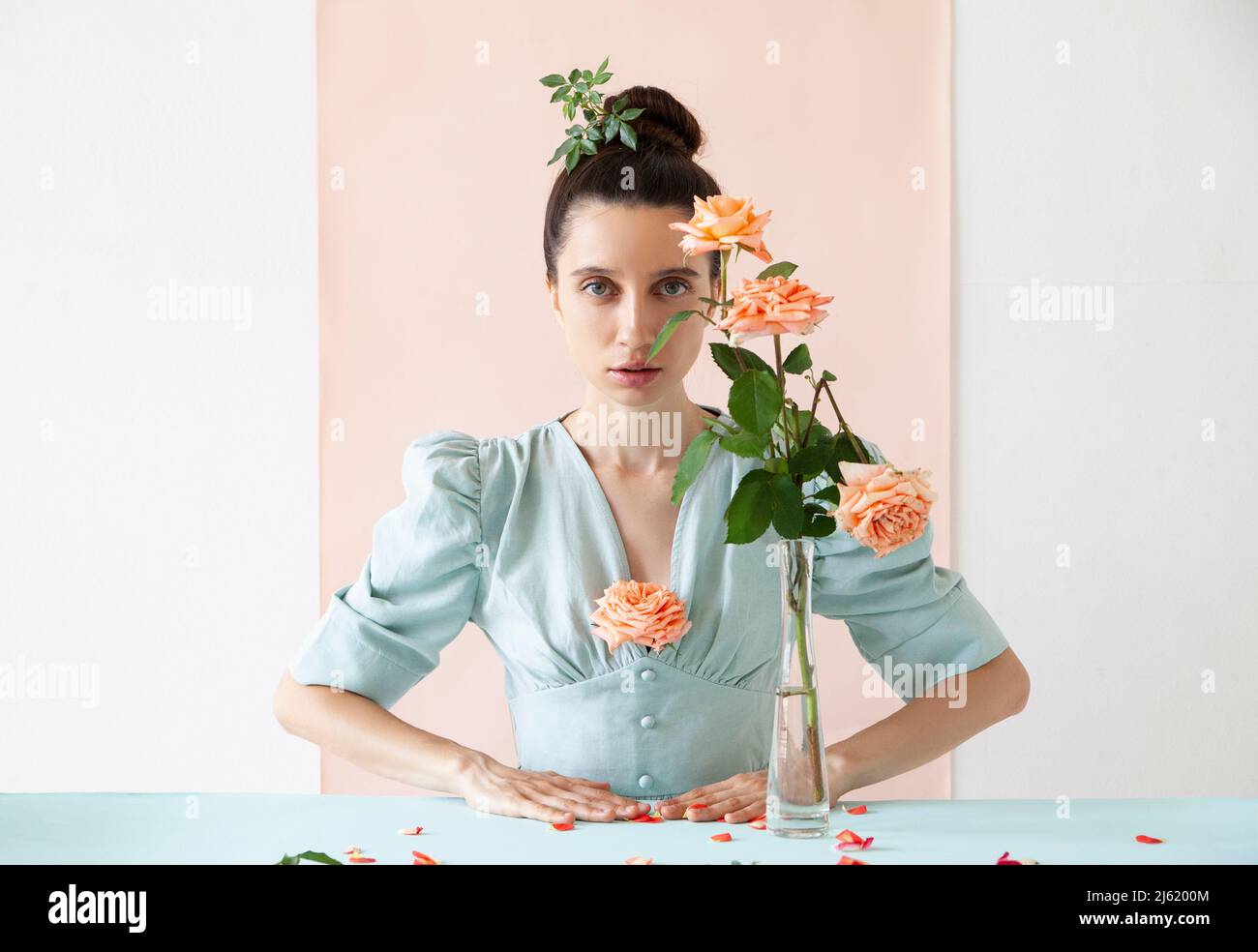 Beautiful young woman with rose in vase against pink backdrop Stock Photo