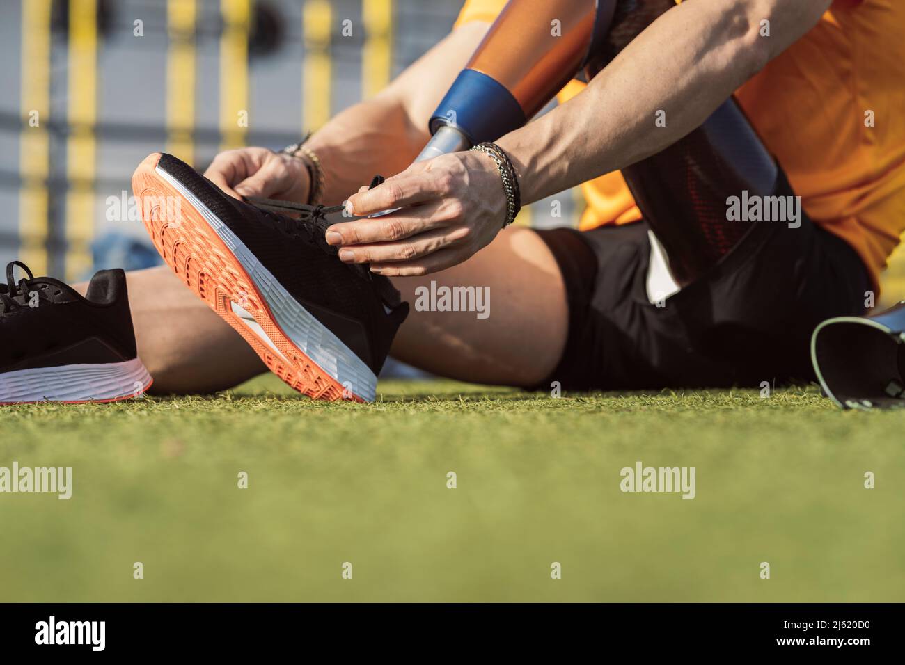 Hands of athlete tying shoelace of prosthetic leg sitting on grass Stock Photo