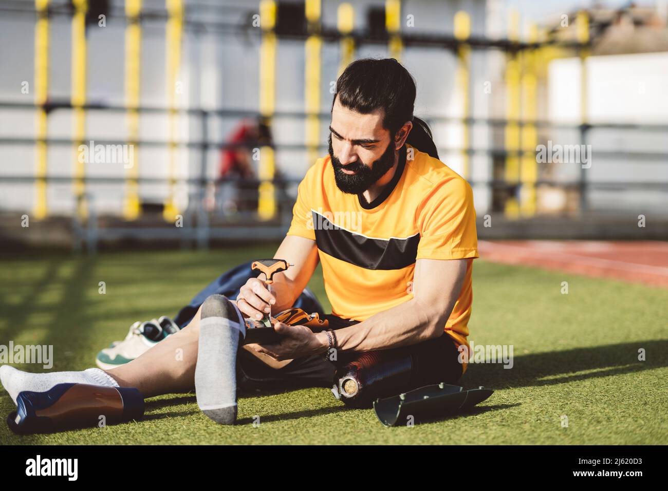 Bearded man adjusting prosthetic leg with screwdriver sitting on grass Stock Photo