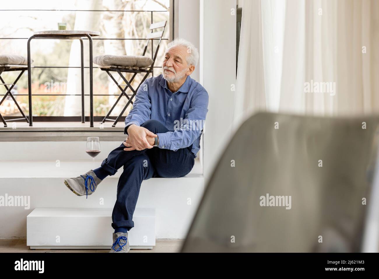 Senior man sitting with legs crossed at knee in front of window at home Stock Photo