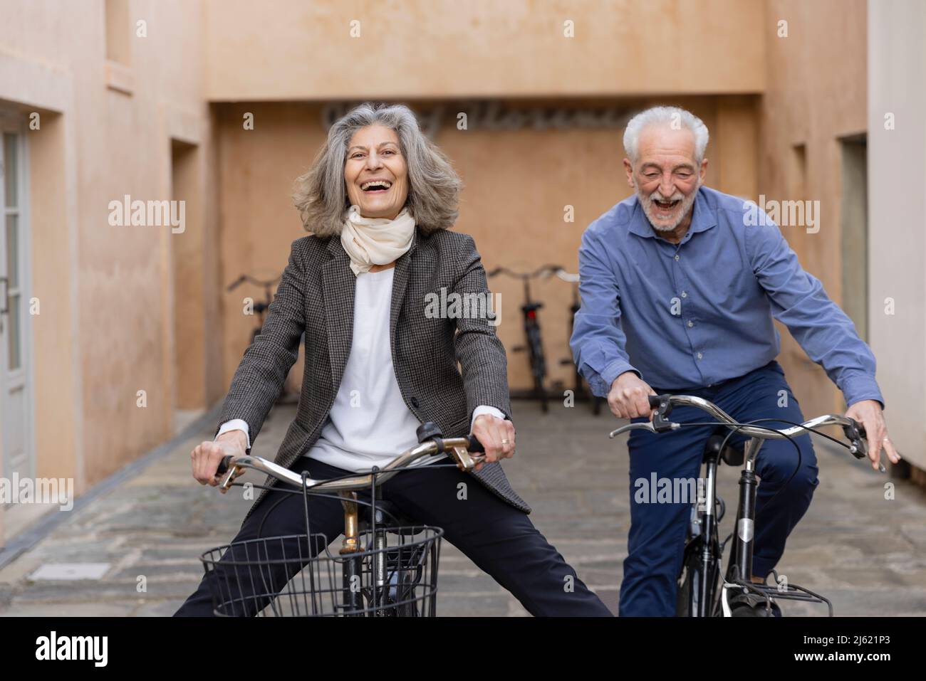 Happy senior couple riding bicycles outside building Stock Photo