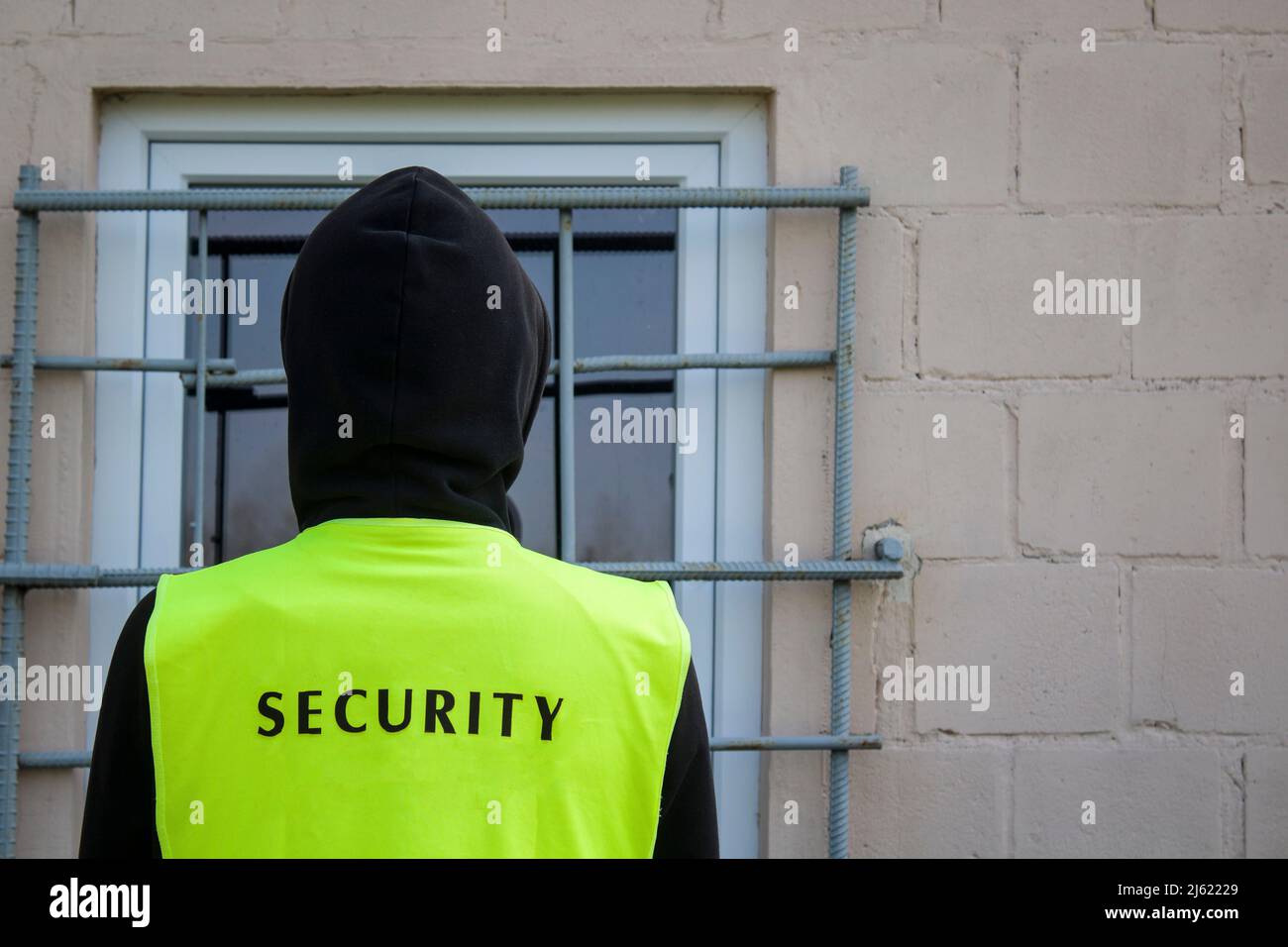 security guard in a yellow vest in front of the barred window Stock Photo
